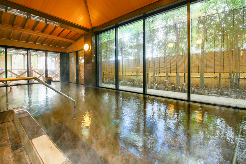 大浴場「光彩の湯」:和風モダンな雰囲気がある広々とした石造りの浴槽で、日中はあざやかな光が射します。窓の外に見える庭の雰囲気もおしゃれです。
